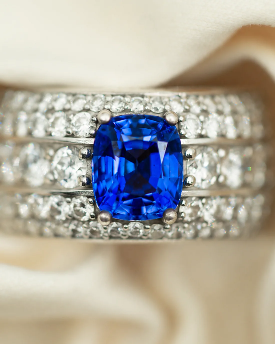 Ceylon cushion sapphire ring with triple-row pavé band on cream silk